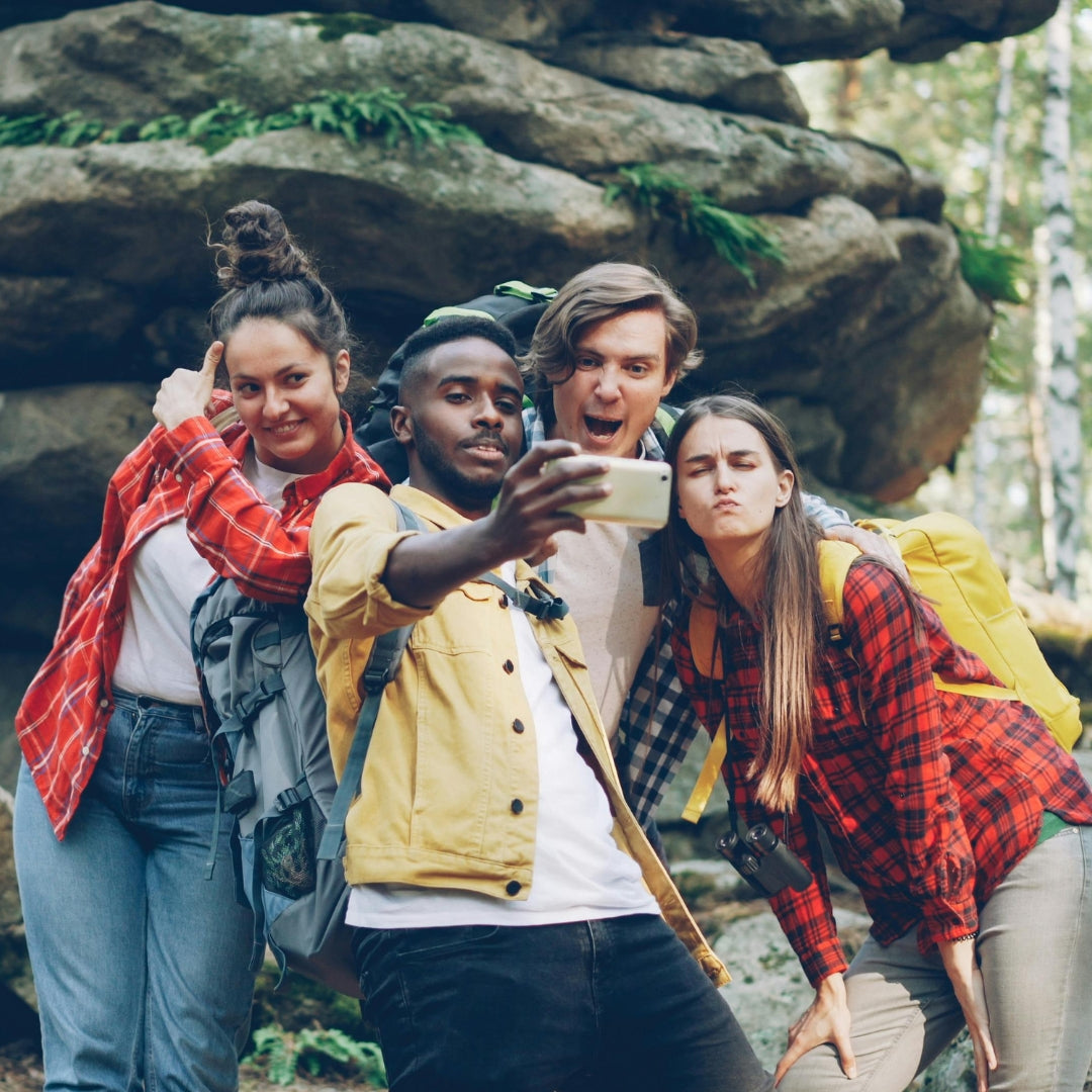 Four friends taking a selfie in a forest with large rocks and trees in the background.